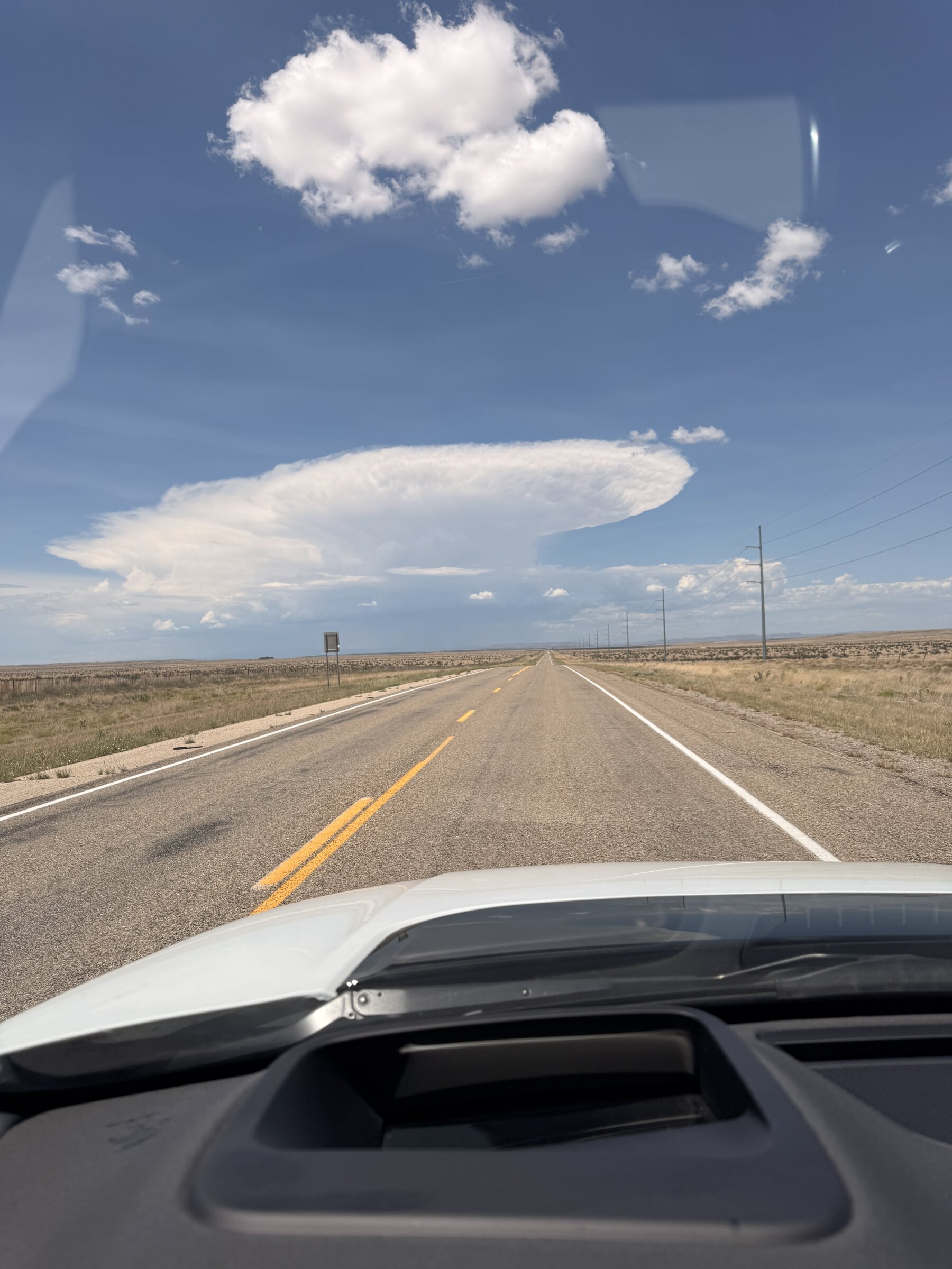 A towering thunderstorm building over the open New Mexico road.